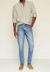 Chemise en lin gris clair boutonnée, jean bleu à jambe droite, et chaussures à enfiler beige. Coupe d écontractée, détails minimalistes, texture lisse.