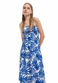 Vestido blanco con patrones de hojas azules, con un cuerpo ajustado y tirantes finos. Presenta una espalda fruncida y una falda fluida para un ajuste relajado.