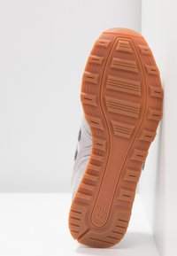 Der Sneaker verfügt über ein strukturiertes graues Obermaterial mit dunklen Akzenten und einer gummierten, orangefarbenen Außensohle. Bemerkenswertes Profil-Design für Grip und Unterstützung.