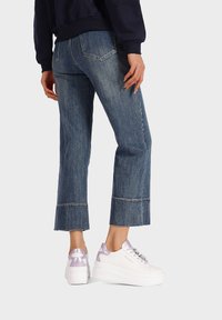 Sneakers platform bianchi con accenti lilla, abbinate a jeans in denim blu scuro a tre quarti con orlo sfilacciato e dettagli di cucitura in evidenza.