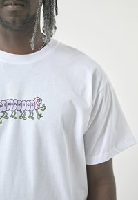 White cotton t-shirt featuring a colorful cartoon caterpillar graphic with purple body segments and green legs on the front.