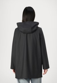 Imperméable noir à capuche avec une texture lisse, coupe ample et longues manches. Design minimaliste, couture visible le long des bords.