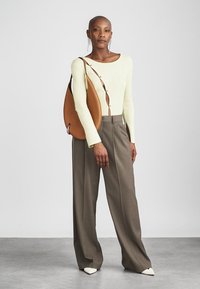 Gaiza zaļa ribota krekla ar garām piedurknēm, kuram ir pogu detaļas, apvienots ar augsto jostasvieta brūnām platām biksēm un brūnu plecu somu.