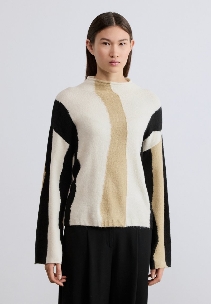 Pull en tricot crème, noir et beige avec des motifs abstraits. Doté d'un col montant et de manches amples. Tissu doux et texturé.
