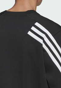 Felpa nera con accenti a righe bianche sulle spalle. Realizzata in un tessuto testurizzato, presenta un collo tondo e maniche raglan.