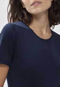 Granatowa dopasowana koszulka z okrągłym dekoltem i krótkimi rękawami. Gładki materiał o subtelnym połysku, z kontrastowymi szwami wzdłuż dekoltu.