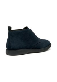 Bottines en daim bleu marine avec une texture lisse, bout rond et semelle en caoutchouc noir. Présente des coutures minimales et une languette pour un enfilage facile.