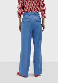 Blue wide-leg trousers with a smooth texture, featuring two back pockets and a tailored waistband. Paired with a patterned red blouse.