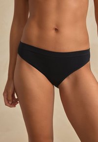 Bas de bikini noir en tissu lisse et extensible avec une couverture minimale et une ceinture élastique. Conçu pour le confort et l'ajustement.
