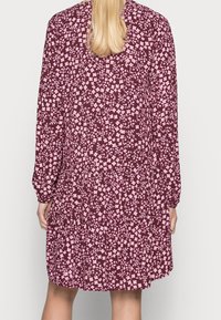 Robe florale avec un fond bordeaux, ornée de petites fleurs roses. Manches longues, taille cintrée et ourlet fluide.
