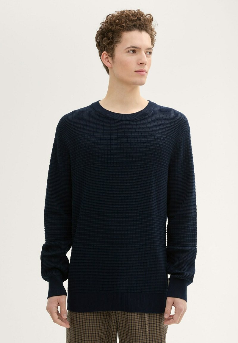 Granatowy sweter dzianinowy z teksturowanym wzorem w siatkę, okrągłym dekoltem i długimi rękawami. Manżety i dół wykończone są ściągaczem.