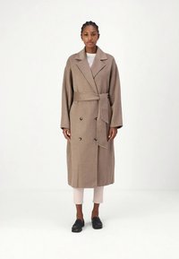 Brauner Wollmischmantel mit Wickeldesign, doppelreihigen Knöpfen und Taillengürtel. Überschnittene Ärmel und knieumspielende Länge.