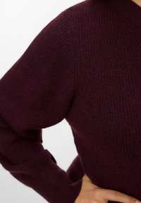 Burgundy stickad tröja med ribbad textur, med en v-ringning och något puffade ärmar. Fokuserar på värme och en avslappnad design.