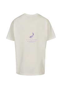 T-majica s kratkimi rokavi, svetlo bež barve, z vijoličnim vzorcem perja in napisom na hrbtni strani, narejena iz mehke bombažne tkanine.