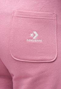 Κοντινό πλάνο σε ροζ υφασμάτινη τσέπη με κεντημένο το λευκό λογότυπο Converse.
