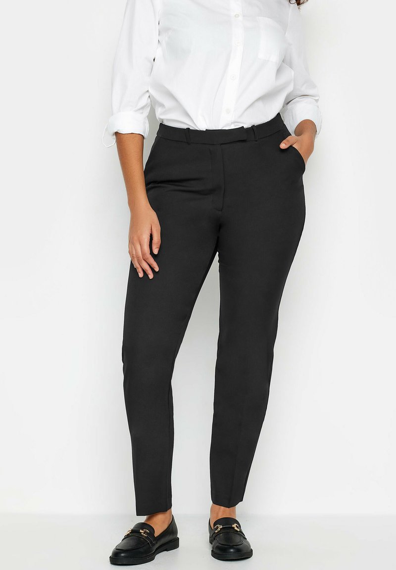 Svarta skräddarsydda byxor med en slät tyg, smal passform och medelhög midja. I kombination med en vit skjorta med knappar och svarta loafers.