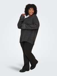 Dark gray knitted sweater with wide cuffs featuring silver studs, paired with black flared pants and black shoes. Side slits in the sweater.