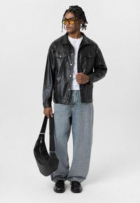 Zwarte leren jas met twee borstzakken, gecombineerd met een wit T-shirt, lichtblauwe losse jeans, zwarte schoenen en een zwarte schoudertas.