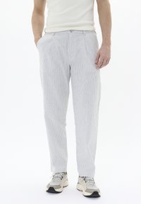 Pantalons légers à rayures bleues et blanches, offrant une coupe ajustée, des plis à l'avant et des poches latérales. Accompagnés de baskets neutres.