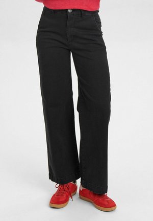 Black wide-leg jeans made from cotton, featuring a high waist, front pockets, and a hem that falls just above red sneakers with a gum sole.
