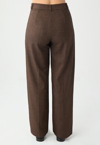 Bruine herringbone broek met een losse pasvorm, hoge taille en achterzakken. Heeft een gladde textuur en iets taps toelopende pijpen bij de zoom.