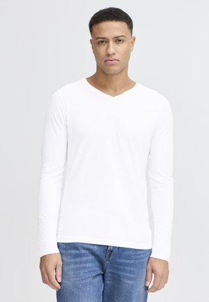 White long-sleeve V-neck shirt with a smooth texture, worn with blue denim jeans. Positioned against a plain light background.