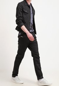 Černá džínová bunda přes šedé tričko s batikovaným vzorem, doplněná černými kalhotami a bílými teniskami. Slim fit design, ležérní vzhled.