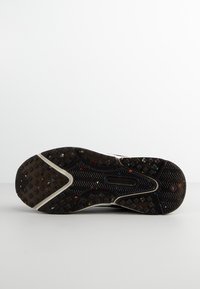 Schwarze Sportschuhsohle mit einer strukturierten, gemusterten Gummifläche; mit bunten Sprenkeln und einem charakteristischen Logo-Detail.