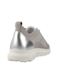 Zapatilla deportiva gris con una parte superior de tejido texturizado, acento de talón metálico plateado y una suela blanca gruesa con patrones en forma de ola.