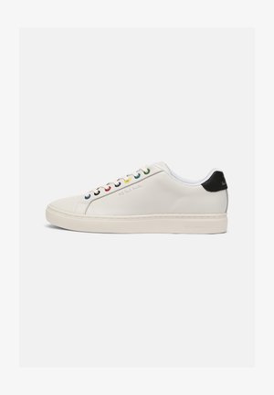 Sneaker en cuir blanc avec un bout légèrement arrondi, semelle plate, œillets multicolores, languette noire au talon et logo en relief sur le côté.