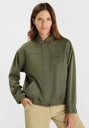 Olive green jacket with a stand collar, side pockets, elastic cuffs, and a logo patch on the chest. Made from a soft textured fabric.