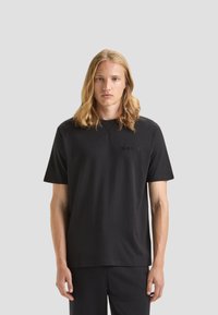 T-shirt in cotone nero con scollatura rotonda e maniche corte. Presenta un logo nero discreto sul petto. Design semplice e dritto.