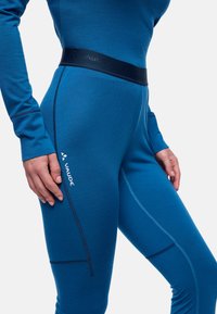 Leggings de sport bleus en tissu lisse, dotés d'une taille foncée, de surpiqûres contrastées et d'un détail de logo sur le côté.