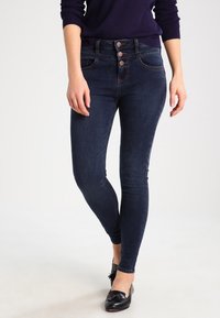 Tummansiniset korkeavyötäröiset skinny-farkut, joissa on kolme nappia ja etutaskut, joissa on sileä denim-kangas ja vartalonmyötäinen muotoilu.