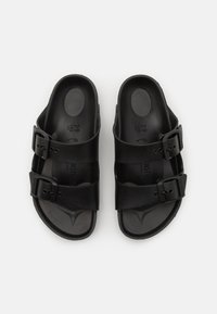 Schwarze Sandalen mit zwei verstellbaren Riemen, aus strukturiertem synthetischem Material, ausgestattet mit einem konturierten Fußbett und flacher, rutschfester Sohle.