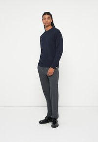 Pull en maille bleu marine associé à un pantalon gris et des chaussures noires. Le pull possède un col rond et un tissu texturé ; le pantalon est ajusté.