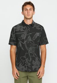 Camisa negra de manga corta con patrones de contorno en blanco de flores y hojas; diseño de botones en la parte delantera y bolsillo de parche en el lado izquierdo.