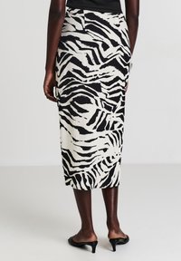 Schwarzer und weißer Zebrastreifen-Bleistiftrock, knielang, strukturierter Stoff, enganliegendes Design, Taillendetail, getragen mit offenen schwarzen Mules.