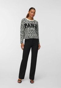 Pull en imprimé léopard avec lettrage noir "PARIS", manches longues, col rond, associé à un pantalon noir à rayures et des sandales noires à lanières.