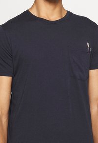 Námořnická modrá bavlněná tričko s krátkým rukávem a kulatým výstřihem. Obsahuje náprsní kapsu s barevným vyšitým motivem zmrzliny.