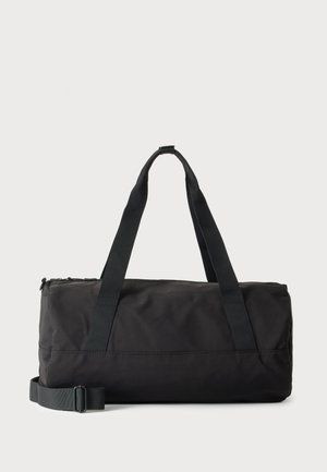 Schwarze rechteckige Reisetasche mit zwei oberen Griffen und verstellbarem Schultergurt auf hellem Hintergrund.