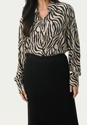 Blusa beige con strisce zebrate nere, maniche lunghe e chiusura con bottoni, abbinata a una gonna nera in maglia testurizzata.