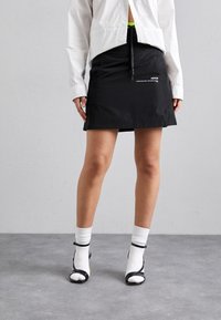 Svart minikjol med dragsko, som har logodetalj. Kombinerad med vita strumpor och svarta sandaler med neondetaljer. Strukturerad tyg.