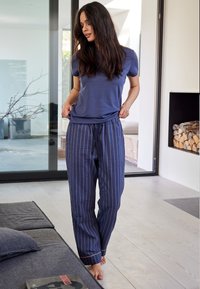 Navy fabric pajama set with short-sleeve top and striped drawstring pants. Soft texture, gold accents on stripes, relaxed fit.