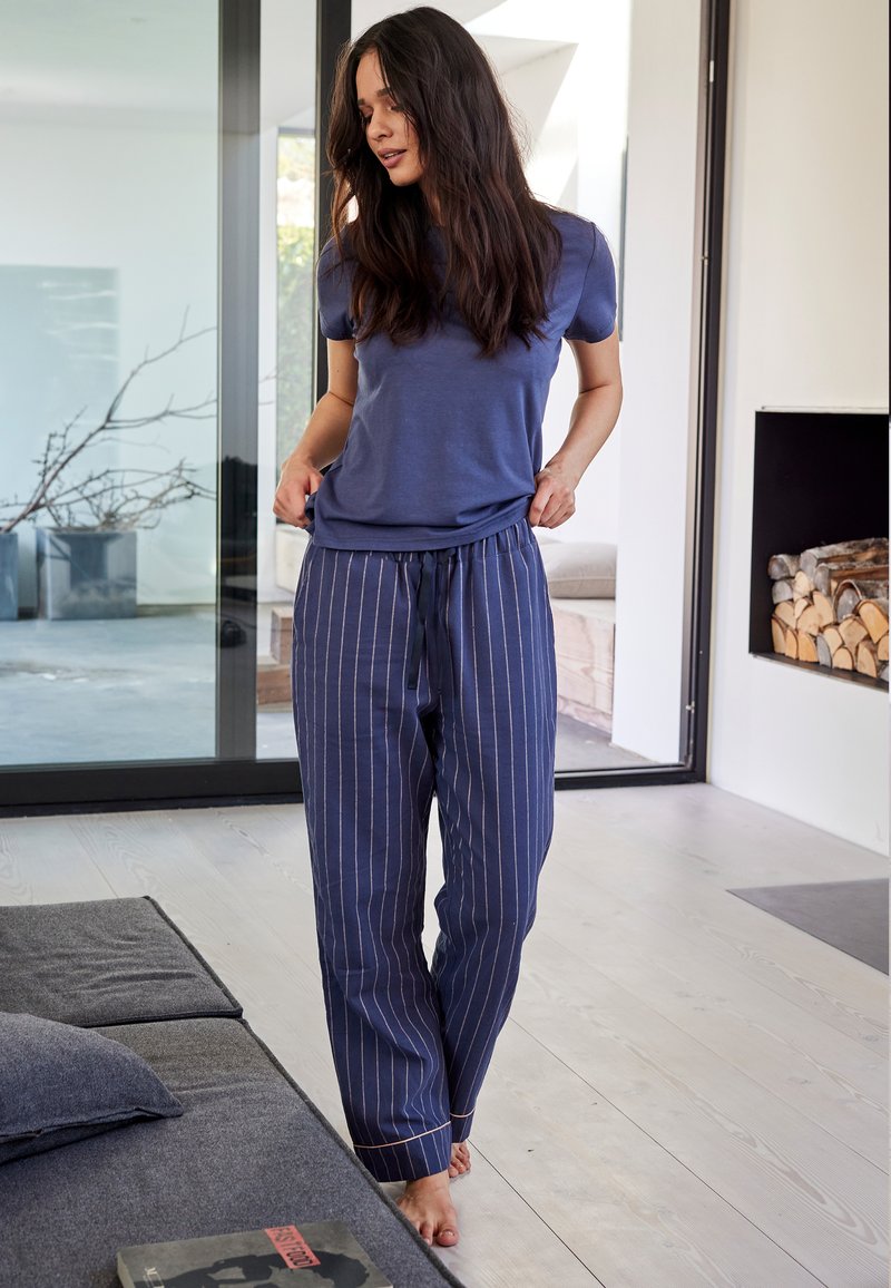 Navy fabric pajama set with short-sleeve top and striped drawstring pants. Soft texture, gold accents on stripes, relaxed fit.