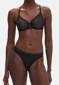 Soutien-gorge en dentelle noire avec armatures et bretelles ajustables, présentant des motifs floraux. Associé à un string en dentelle assorti, également noir, avec un bord festonné.