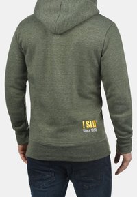 Felpa verde realizzata in tessuto testurizzato, dotata di un ampio cappuccio e di un logo giallo con "SLD Since 1993" nella parte bassa della schiena.