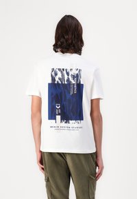 Hvit bomulls T-skjorte med et blått grafisk design på baksiden, med abstrakte mønstre og tekst, kortermet og avslappet passform.
