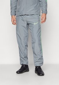 Graue Nike Jogginghose mit slim Fit, ausgestattet mit neongrünen Seitenstreifen und Logo. Hergestellt aus glattem, leichtem Material.