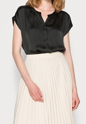 Schwarze Satinbluse mit V-Ausschnitt und kurzen Ärmeln, kombiniert mit einem cremefarbenen Faltenrock mit elastischem Bund.
